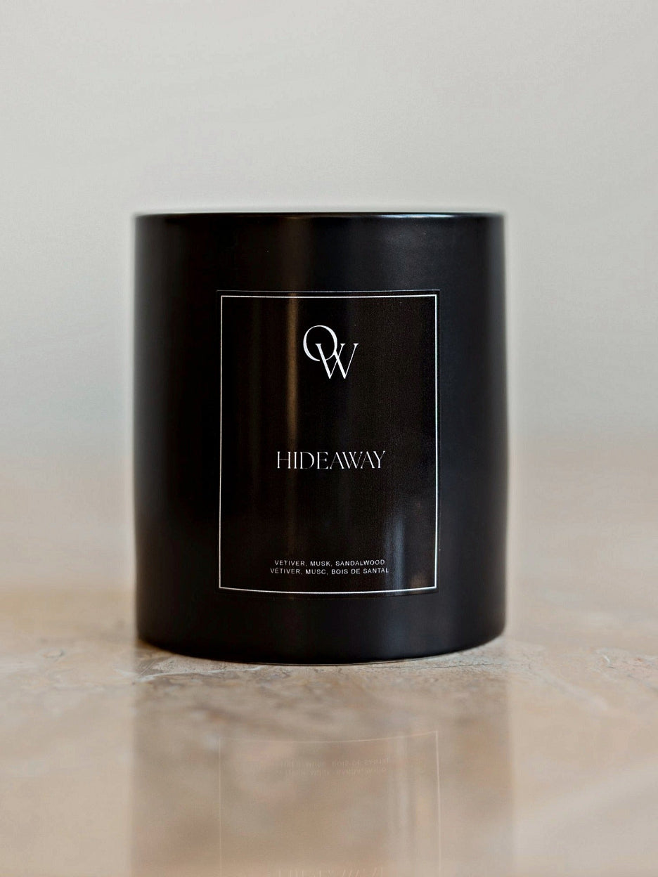 One Wednesday Hideaway soy candle in a black vessel on a pale stone surface.