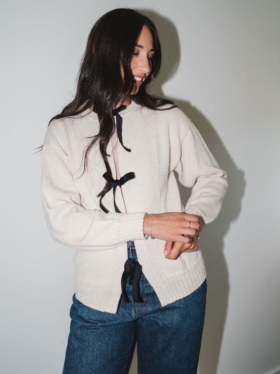 Model wearing the cream Bow Knit baby alpaca sweater with black ribbon bows, styled with blue jeans