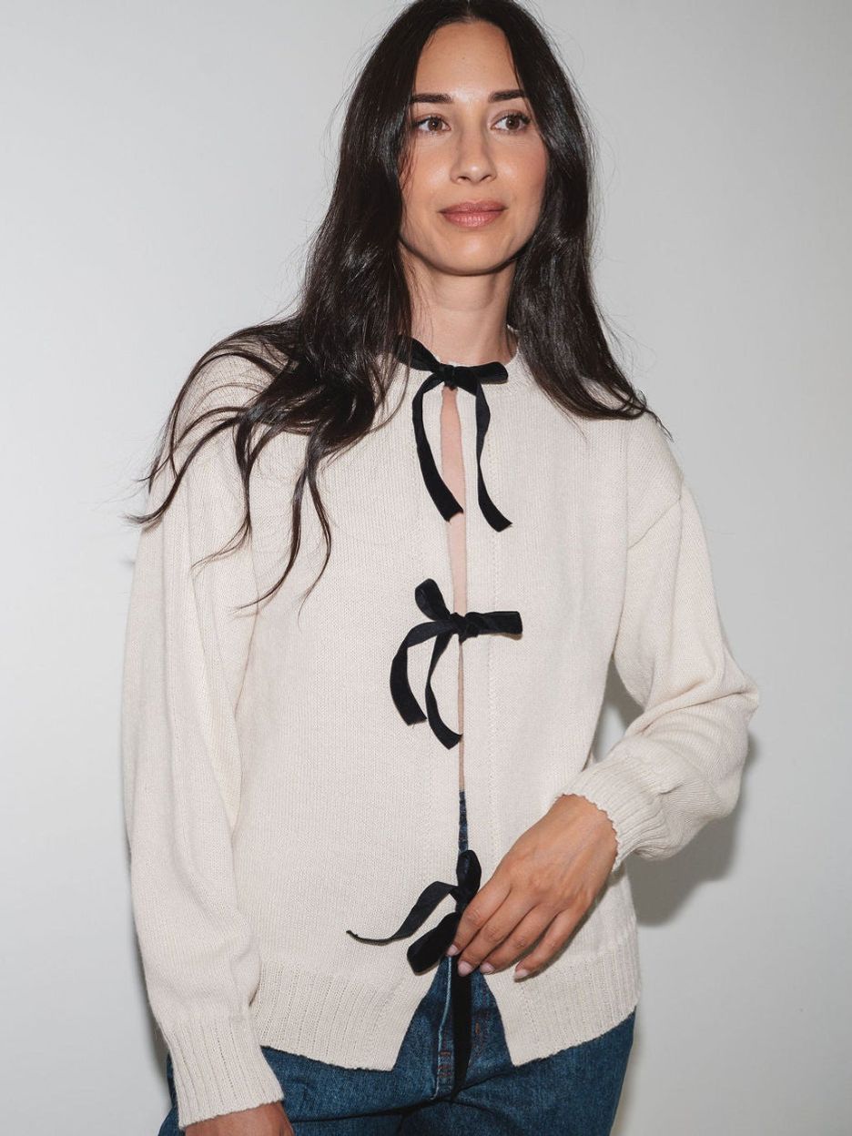Front view of the cream Bow Knit sweater showing black velvet ribbon bows at the neckline, waist and hem