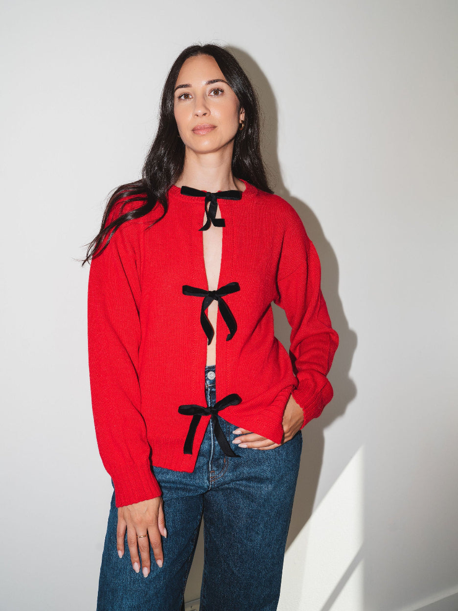 Model wearing the red Bow Knit baby alpaca sweater with black ribbon bows down the front