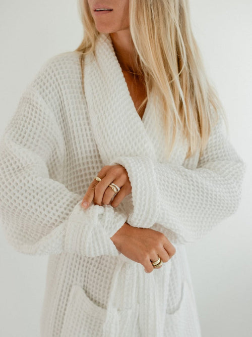 Woman leaning against a wall wearing the butter Waffle Knit Robe with belt tied