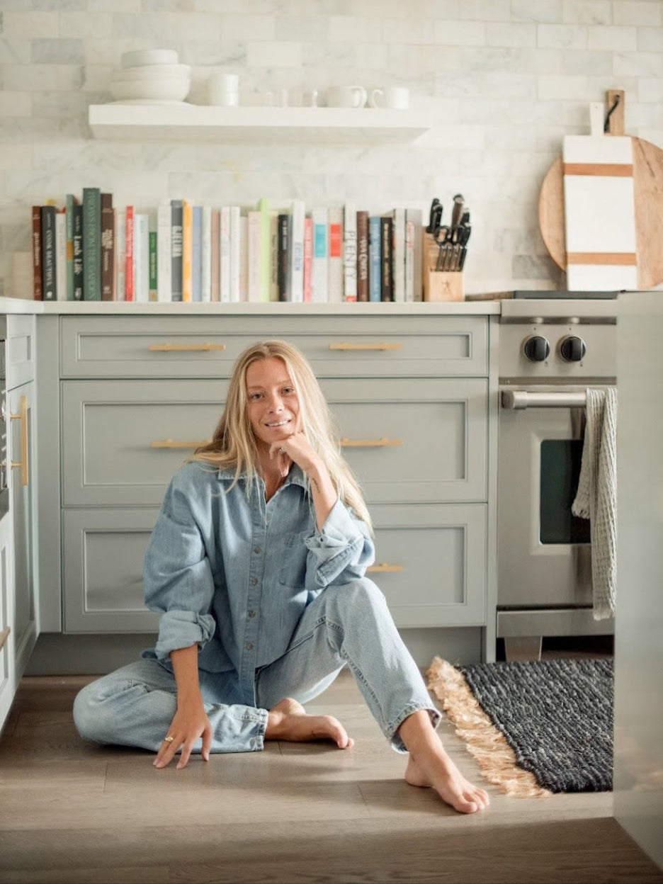 One Wednesday blue chambray shirt styled with light-wash jeans, worn by a model seated beside kitchen cabinets.