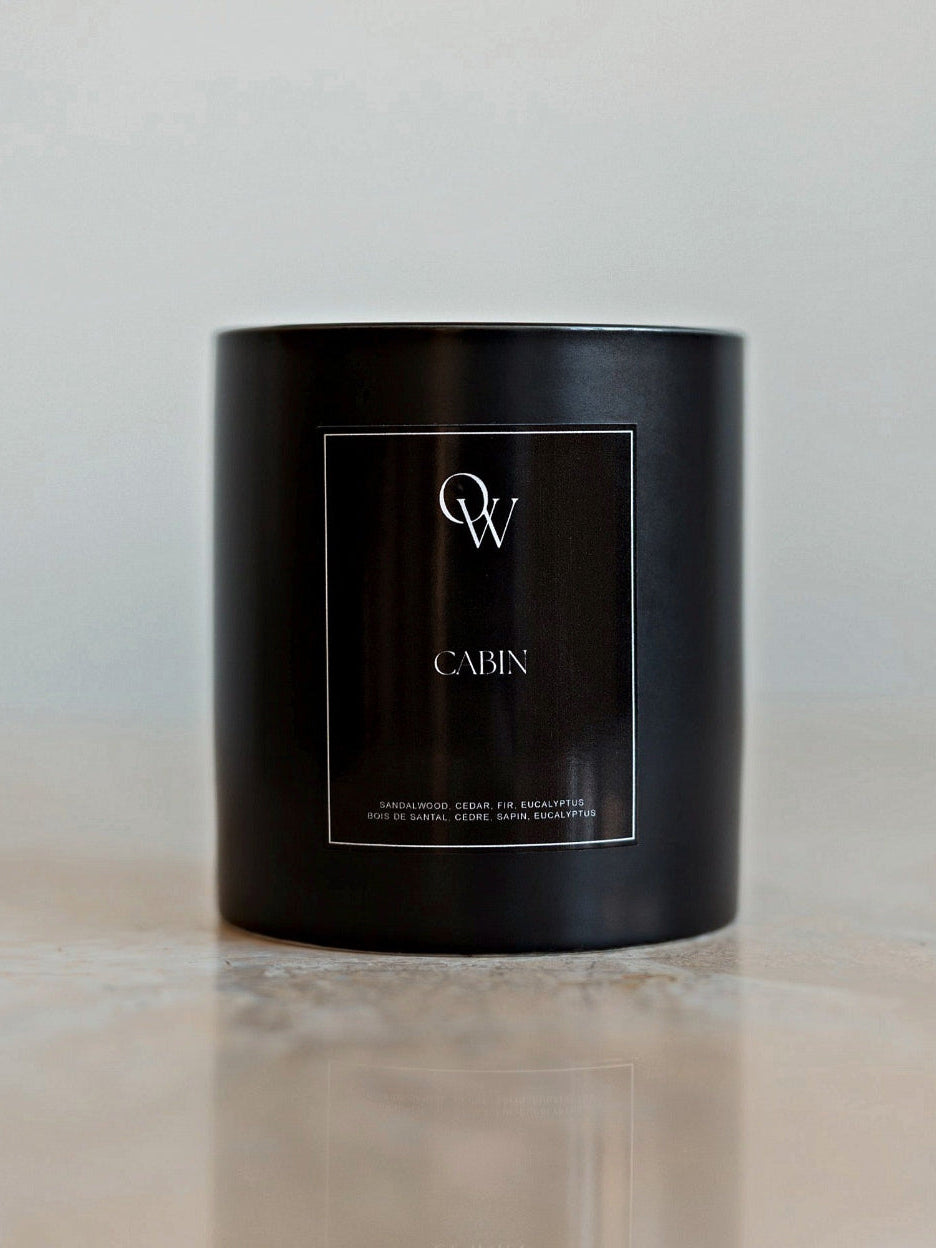 One Wednesday Cabin soy candle in a black vessel on a pale stone surface.